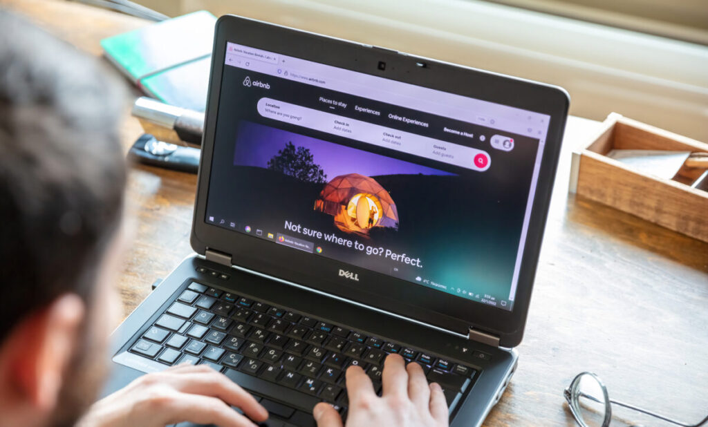 Man utilizes a laptop to browse Airbnb for accommodation options