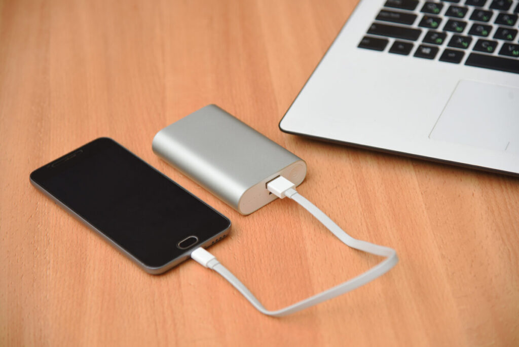 Wooden table featuring a smartphone, laptop, and a charger power bank