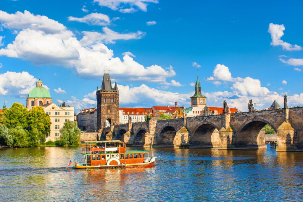 Boat in Vltava river sailing across the Charles Bridge in Prague, Czech Republic