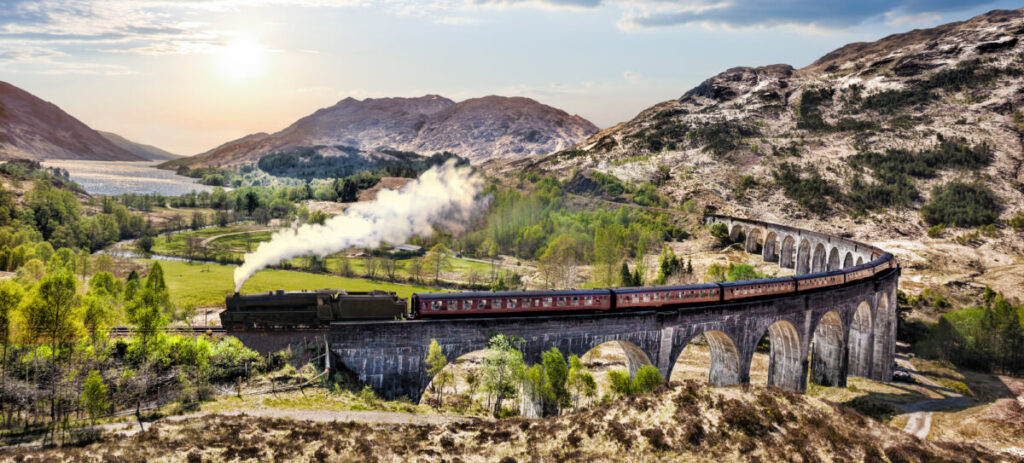 Panoramic viewa train passing by the Glenfinnan Railway Viaduct in Scotland