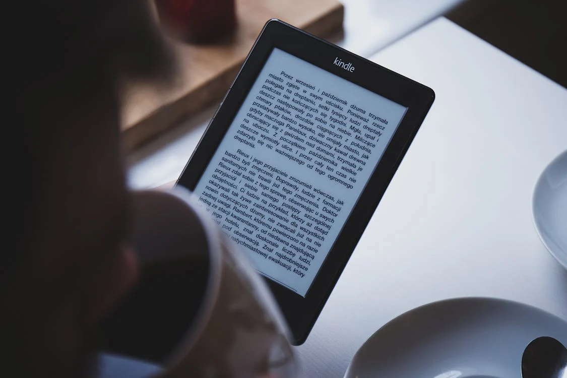 Person Using E-book Reader While Drinking Coffee
