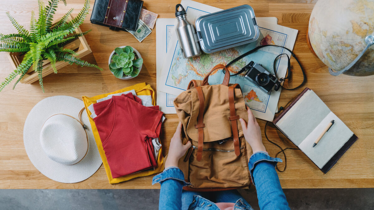 Woman preparing a backpack, clothes, and other travel essentials for travel packing