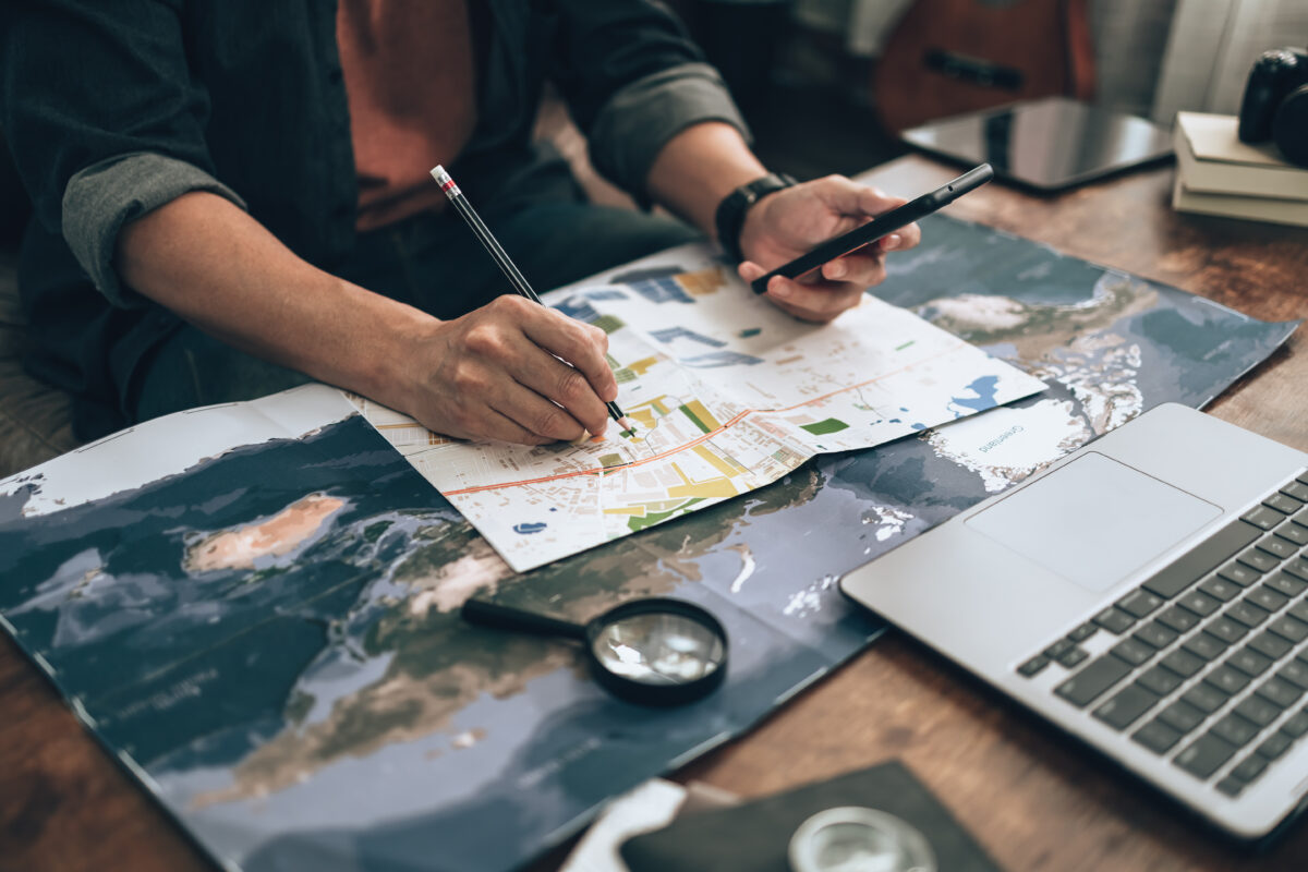 Man planning his travels with a phone, map, pen, and various travel essentials