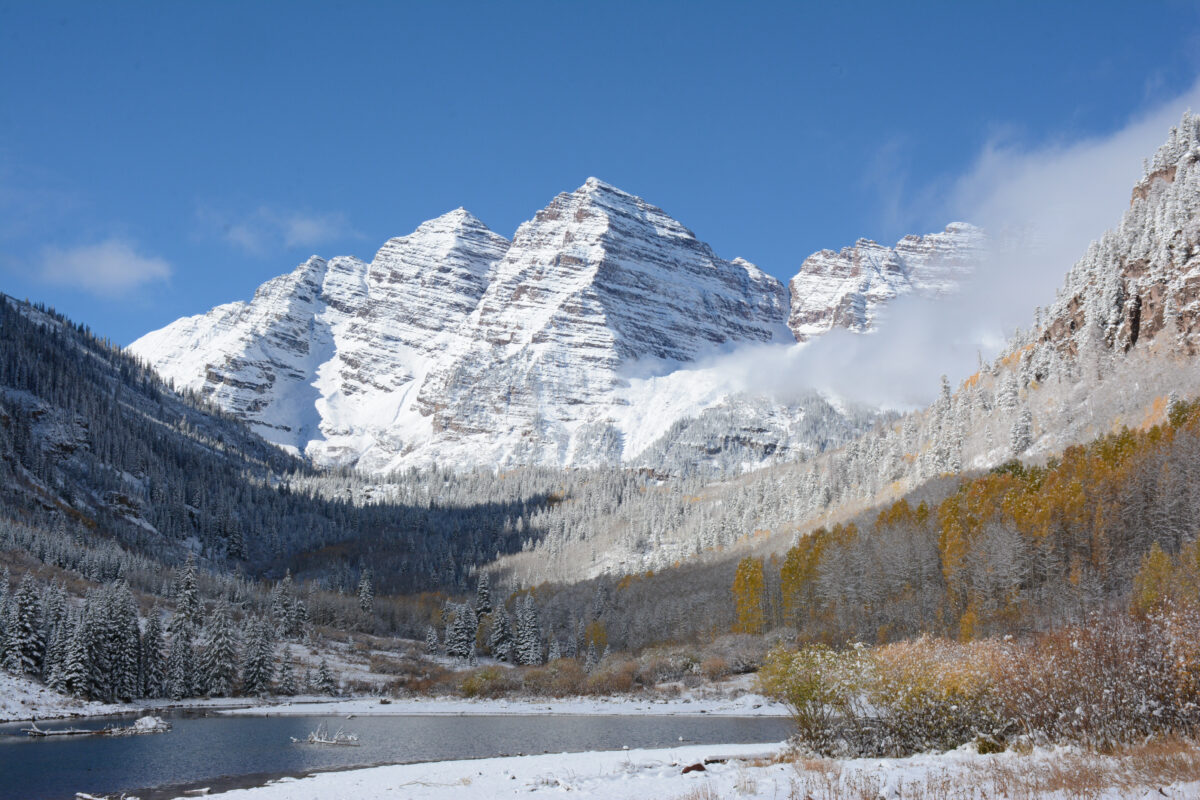 The iconic Maroon Bells reflected in Maroon Lake with families hiking along the accessible trail in autumn with golden aspen trees