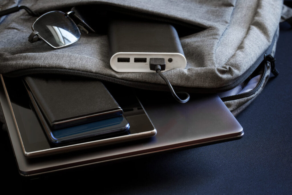 Travel gadgets, including a smartphone, tablet, and portable charger, placed on a travel backpack