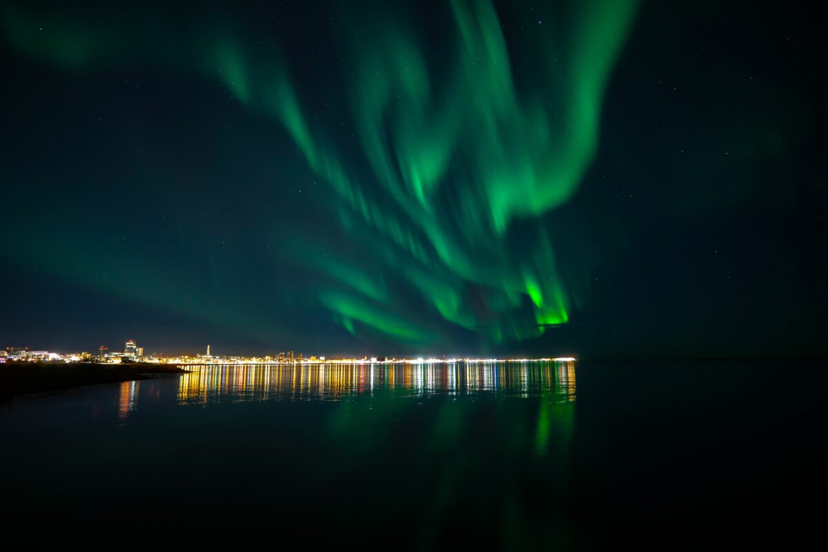 Beautiful scene of the turquoise northern lights reflected in the ocean in Reykjavik, Iceland