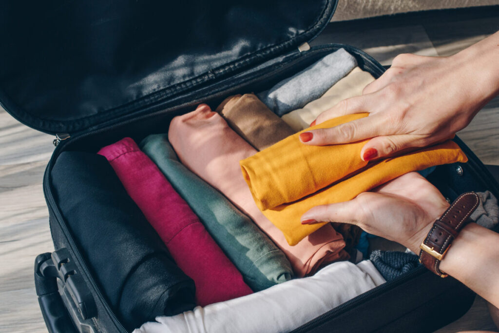 Close-up of a woman's hands rolling clothes to efficiently pack them into a suitcase for an upcoming trip