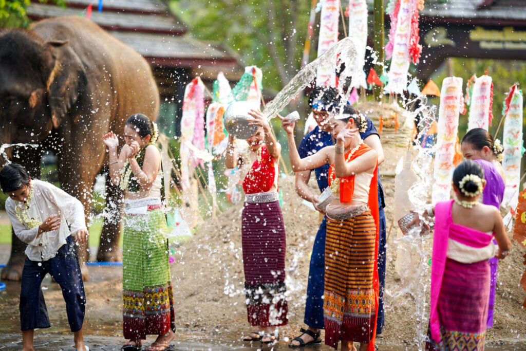 Thai women and children gathered near an elephant playfully splashing water, joyfully celebrating the Songkran Festival in Thailand