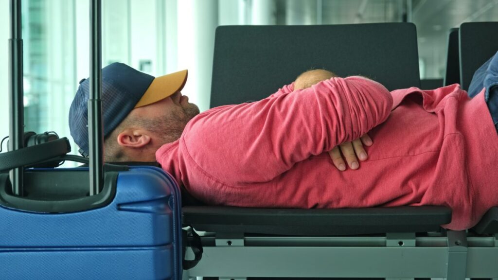 Tired male passenger with a jet lag napping on an Airport terminal bench