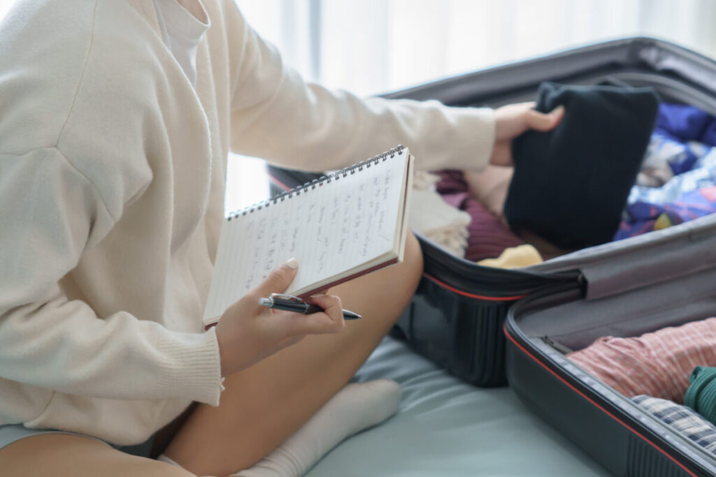 Woman packing a suitcase on a bed while using a checklist