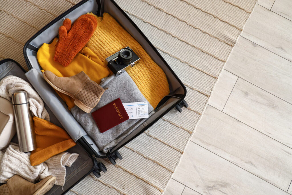 Open suitcase displaying winter clothes and travel accessories arranged on a carpet