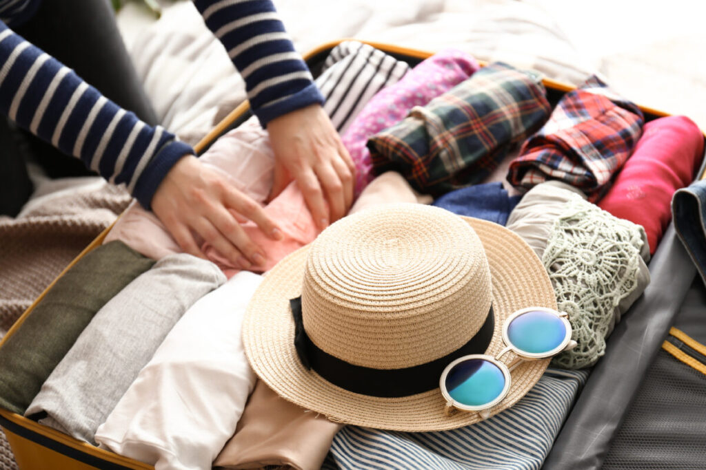 Young woman packing suitcase  with sunglasses and hat at home for a vacation travel